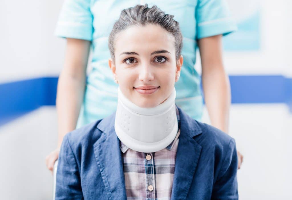 Professional nurse pushing a young smiling female patient on wheelchair with cervical collar