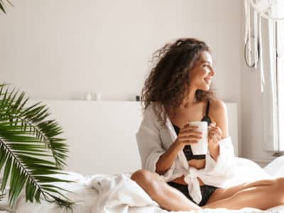 woman wearing lingerie smiling and drinking tea on bed