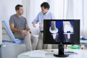 Orthopaedic surgeon discussing knee replacement options with a patient while reviewing knee implant images on a monitor.